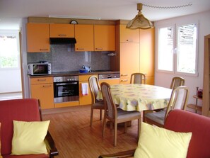 Eine kompakte Küche mit Mikrowelle, Backofen und Spüle, Holzstühlen und einem Esstisch mit gelber Tischdecke.