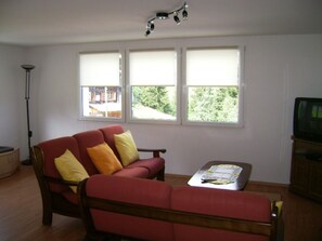 Ein Wohnzimmer mit einem roten Sofa, einem Holztisch und einem Fernseher.