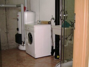 Een kleine badkamer met een wasmachine, een wastafel en een douche.