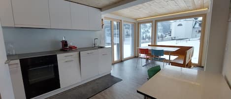 A modern kitchen with white cabinets, a built-in oven, and a dining area with a table and chairs.