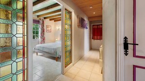 A hallway with a bed, a door with a black handle, and a stained glass window. - Gîte La Bergerie – With Pool! (Saint-Michel-en-l'Herm)