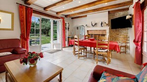 A room with a wooden ceiling, a dining table with chairs, a sofa, and a TV mounted on the wall. - Gîte La Bergerie – With Pool! (Saint-Michel-en-l'Herm)