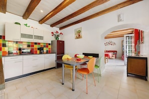 Een keuken met witte kasten, een betegelde achterwand en een eethoek met een tafel en stoelen.