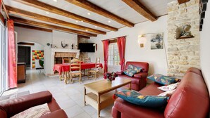 A living room with a fireplace, red leather sofas, a wooden coffee table, and a stone wall. - Gîte La Bergerie – With Pool! (Saint-Michel-en-l'Herm)