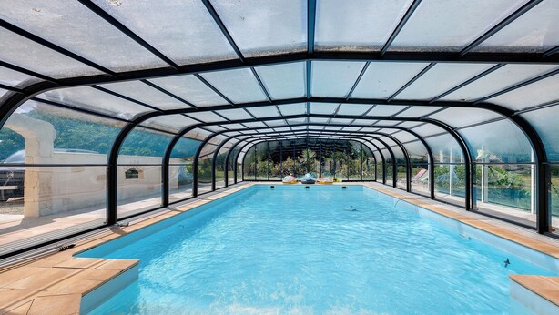 An indoor swimming pool with a glass ceiling, clear water, and a view of the surrounding landscape. - Gîte La Bergerie – With Pool! (Saint-Michel-en-l'Herm)