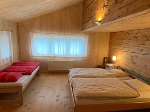 Une chambre avec deux lits, une fenêtre avec des rideaux légers, un radiateur et des murs en bois.