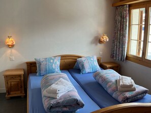 Un lit double avec des oreillers assortis et une table de chevet, une lampe fixée au mur et une fenêtre avec des rideaux.