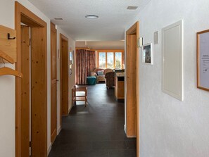 A hallway with wooden doors, a dining area with a table and chairs, and a kitchen area with cabinets. - Casa Mulinera 1 GVH, (Camischolas/Sedrun), 243.01 by Interhome (Camischolas)