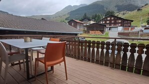 Een houten terras met een tafel en stoelen, met uitzicht op een berglandschap met gebouwen.