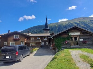 Ein Berggasthof mit Kirchturm, einem Geschäft und einem parkenden Auto.
