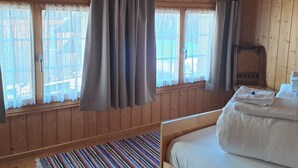 Een houten kamer met een bed, een raam met gordijnen en een klein tafeltje met handdoeken.