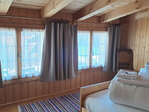 Ein Holzhütten-Zimmer mit einem Bett, einem Fenster mit Vorhängen und einem kleinen Tisch mit Handtüchern.