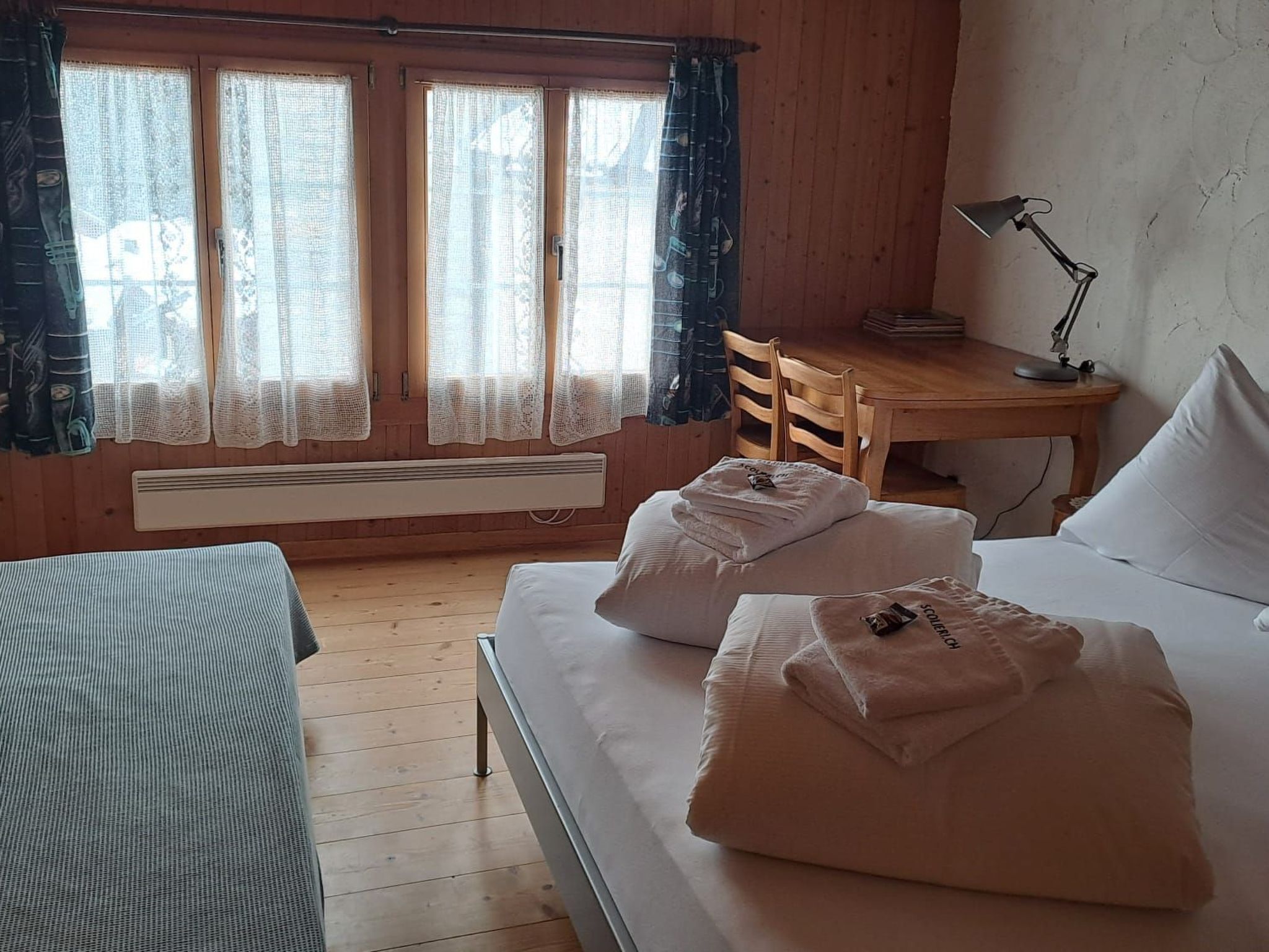 A room with a bed, a desk, a chair, and a window with curtains.