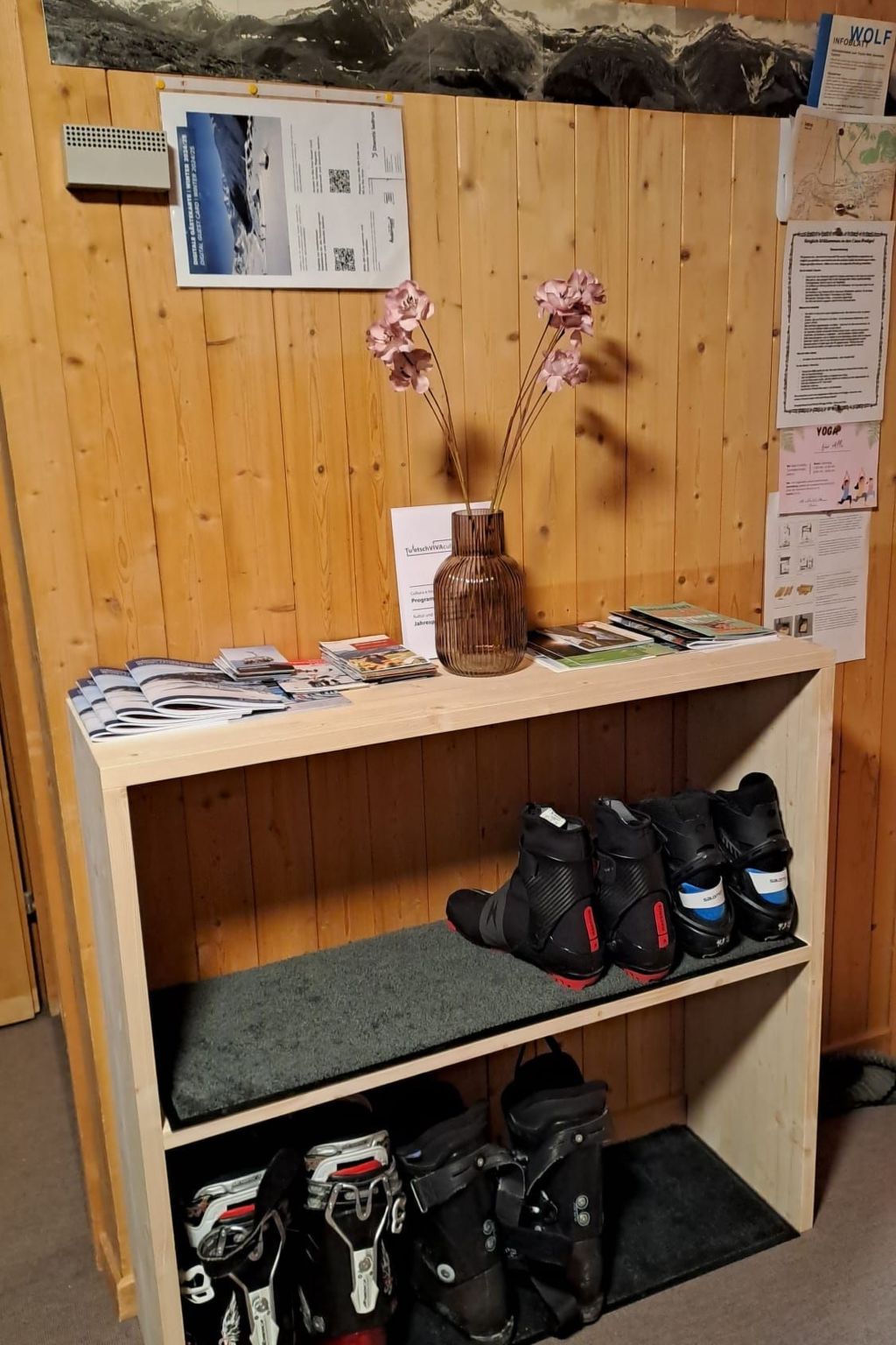 Een houten plank met tijdschriften, een vaas met bloemen en een paar laarzen.