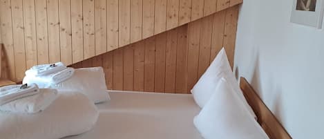 A neatly made bed with white linens and pillows, a wooden headboard, and a wooden sloped ceiling.