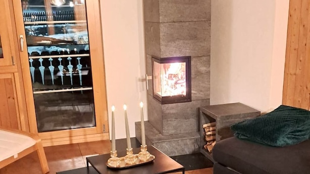 Een woonkamer met een stenen open haard, een glazen deur naar een balkon en een donkergrijze bank.