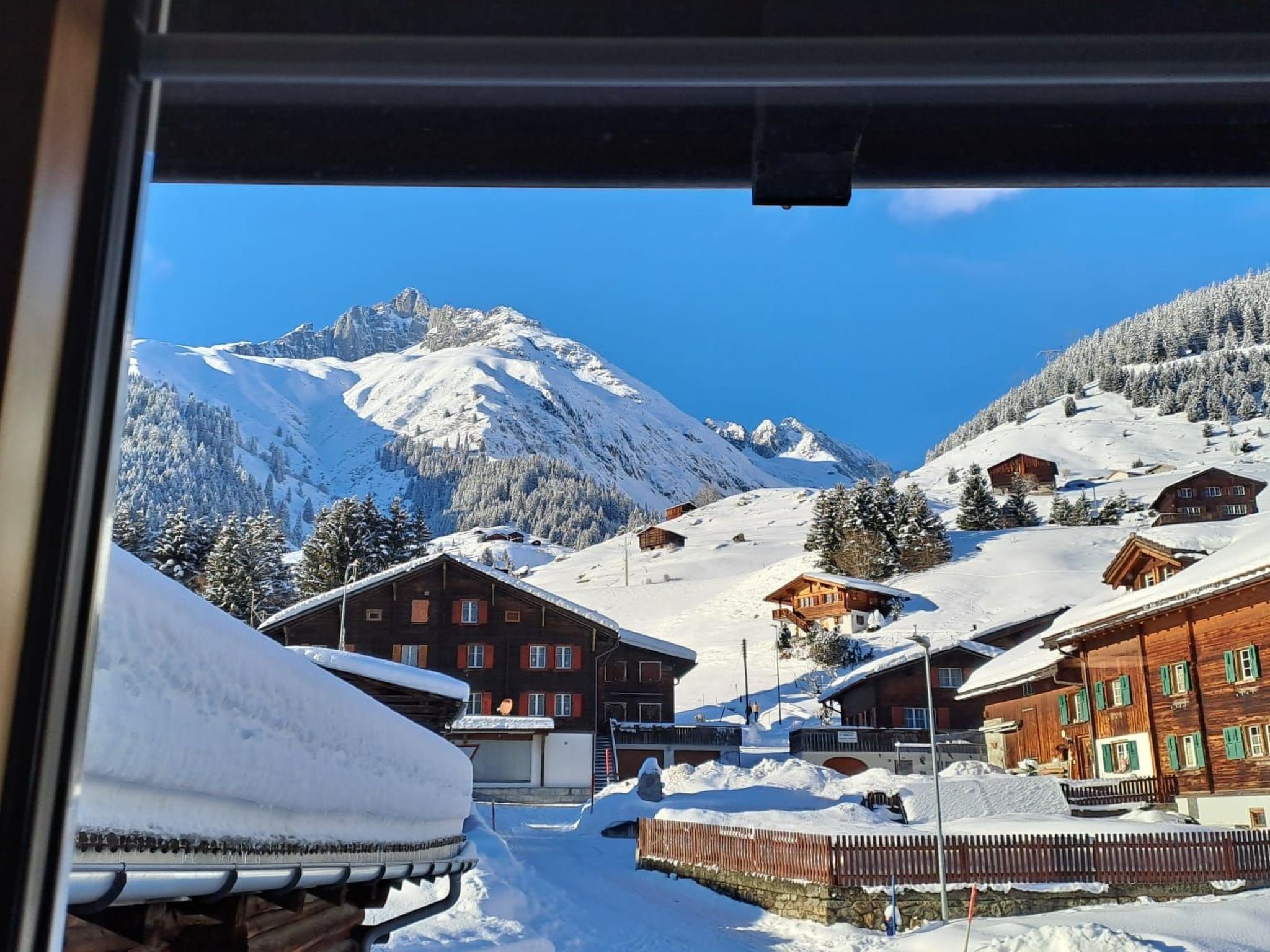 Un pueblo cubierto de nieve en la montaña, con edificios de madera tradicionales y un cielo azul despejado.