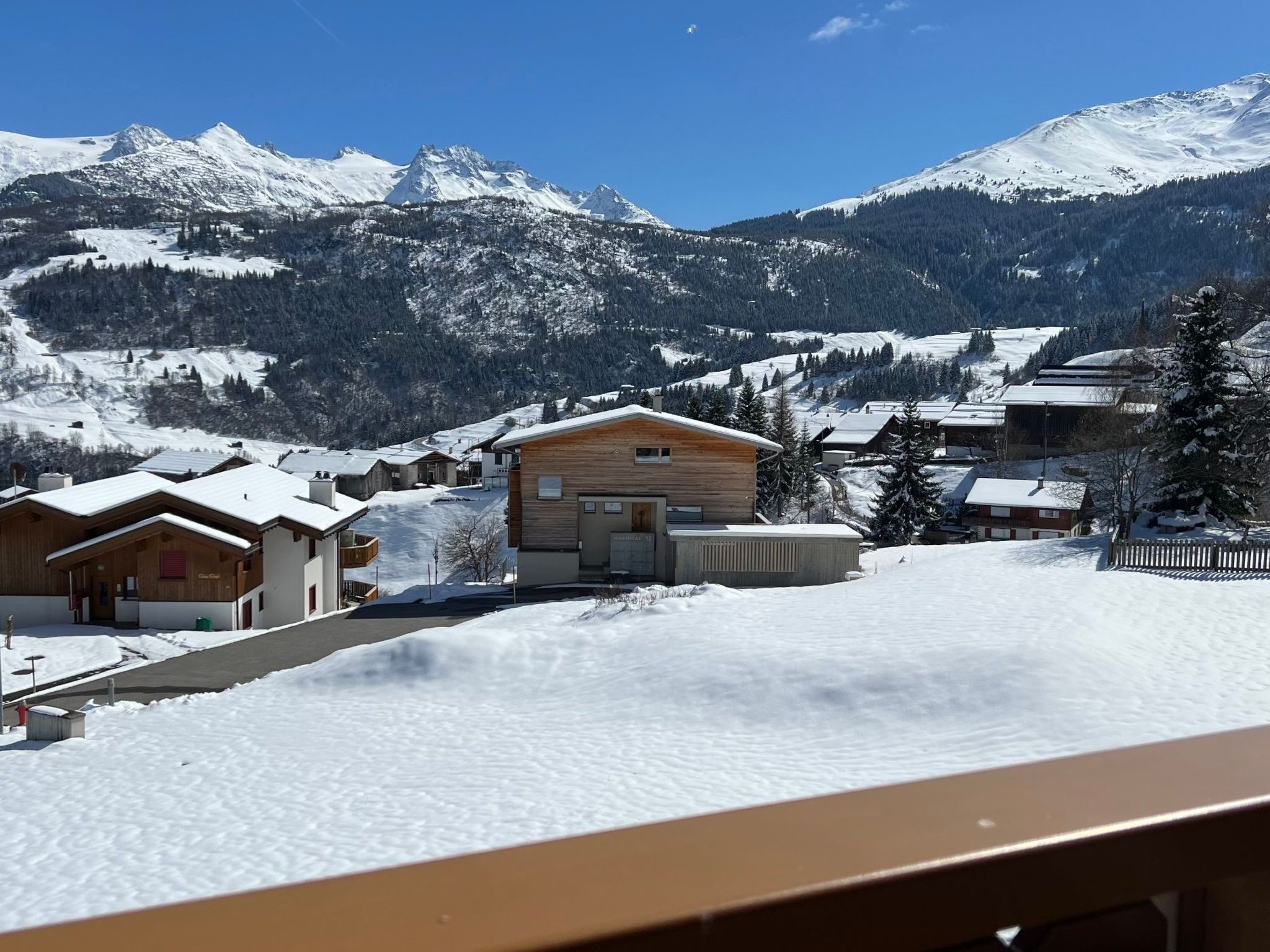 Un village de montagne enneigé, avec des bâtiments en bois et un ciel dégagé.
