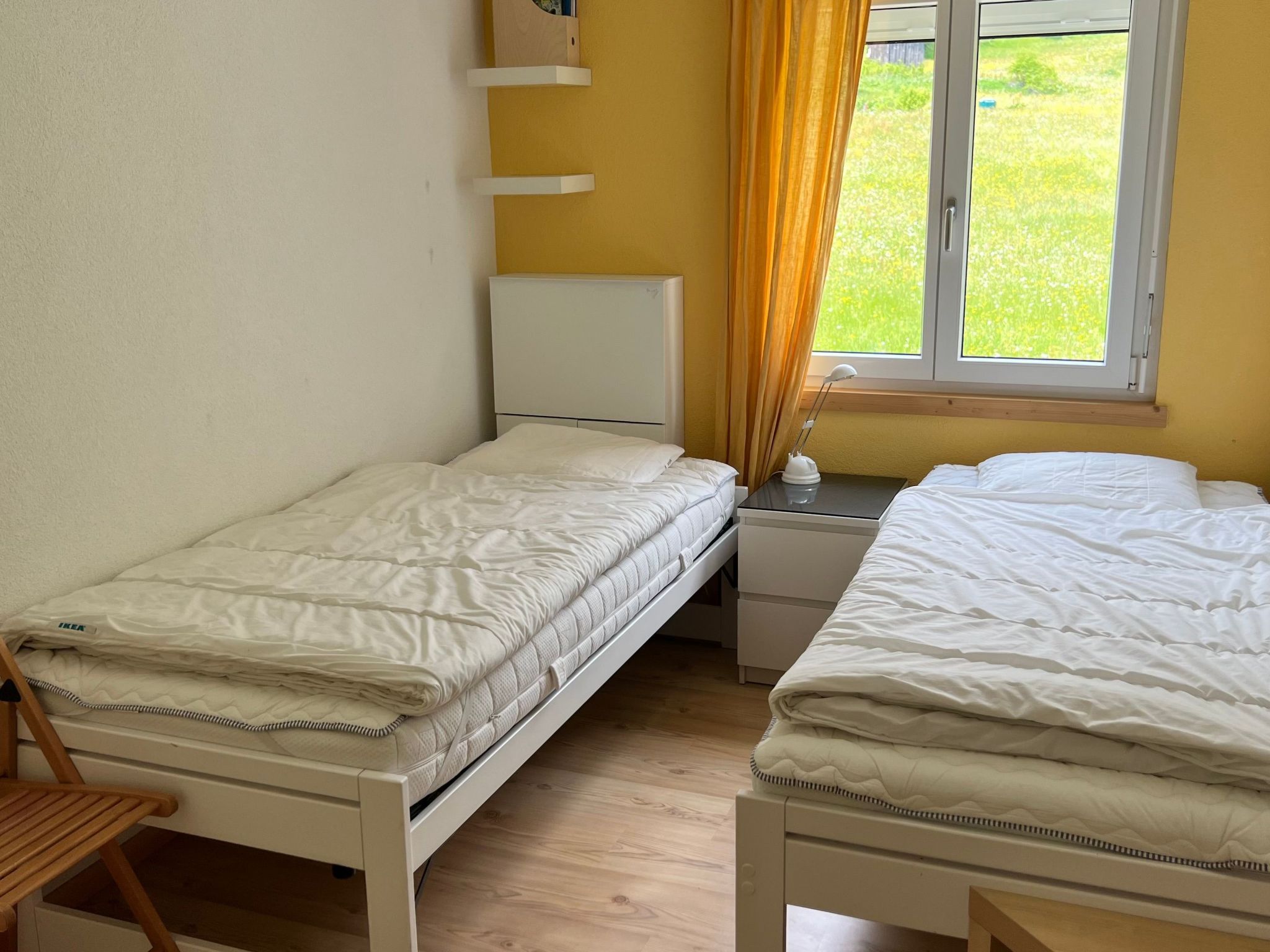 A small room with two single beds, a nightstand with a lamp, and a window with curtains.