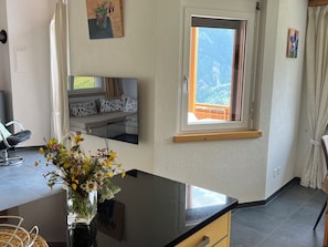 Ein Zimmer mit großem Fenster, einer Couch mit gemusterten Kissen, einer schwarzen Arbeitsplatte und einer Vase mit Blumen.