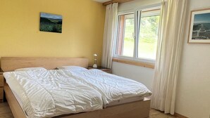 A bed with a wooden headboard, a bedside table with a lamp, a window with curtains, and a picture on the wall. - Casa Diala Panorama, (Segnas/Disentis), 1106 by Interhome (Disentis)