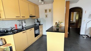 A modern kitchen with yellow cabinets, a black countertop, and a small island. There is a sink, stove, and various kitchen utensils. A vase with flowers is on the island. - Casa Diala Panorama, (Segnas/Disentis), 1106 by Interhome (Disentis)