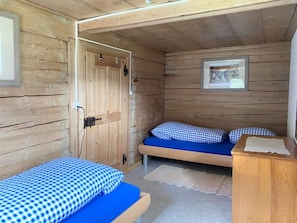 A wooden cabin room with two beds, a door, and a small table. - Casa Gion Giusep Cavegn, (Rueras Sedrun), 703.01 by Interhome (Rueras Dieni)
