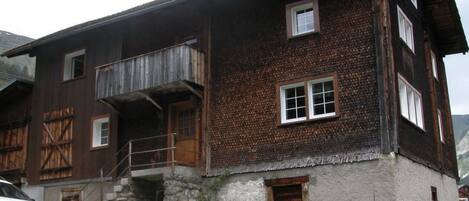 Et traditionelt træhus med balkon, støtten fundament og en bil foran.