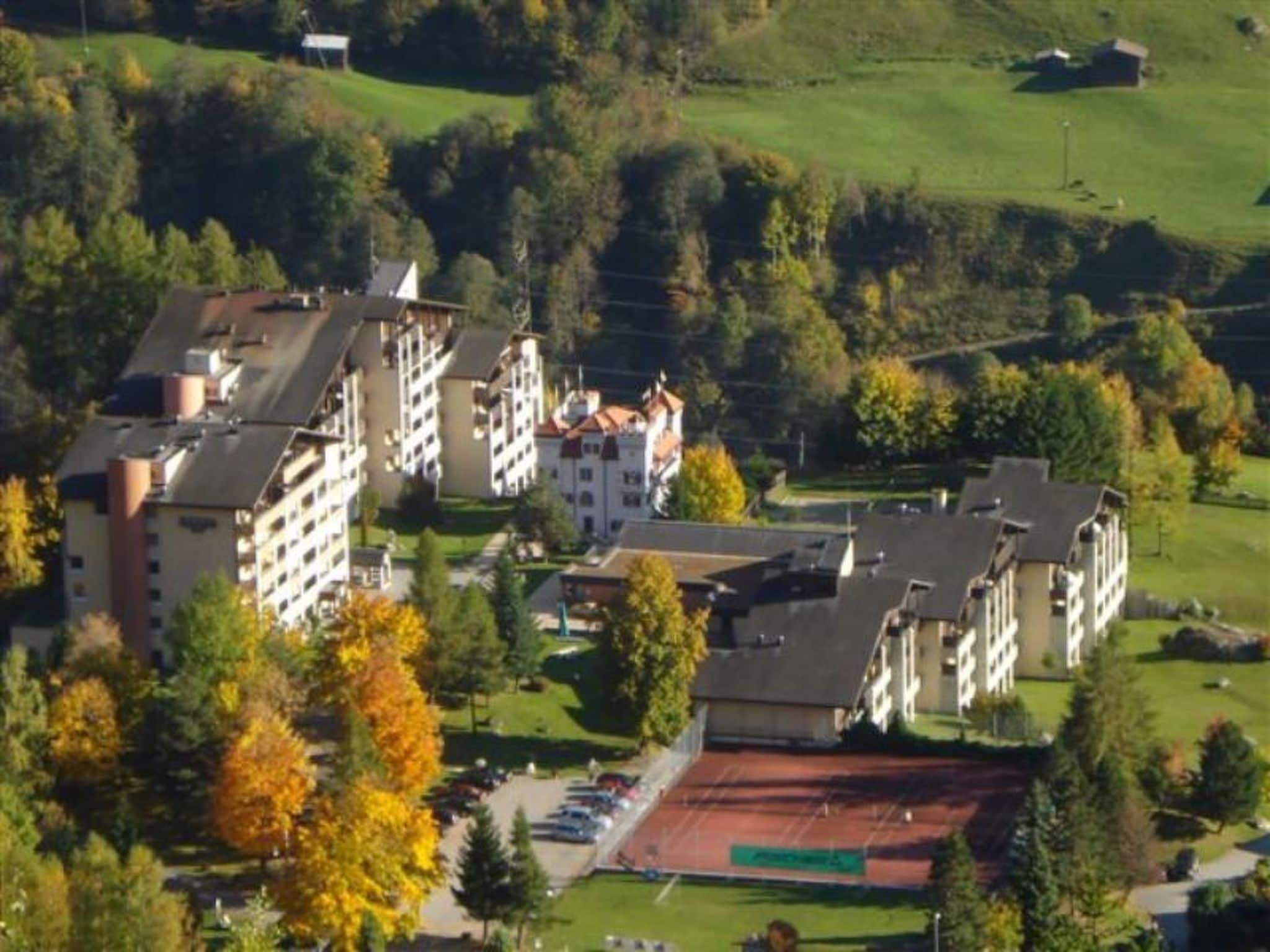 A multi-story hotel with a central courtyard, surrounded by trees and a green field.