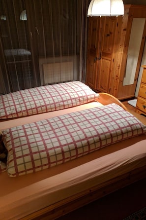 Een kamer met twee bedden, elk met een geruit kussen, een houten garderobe en een spiegel.