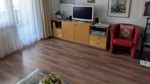 Ein Wohnzimmer mit Fernseher, Holzschränken, einem roten Sessel und Bildern an der Wand.