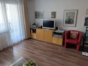 A living room with a flat-screen TV, wooden cabinets, a red armchair, and artwork on the wall. - Disentiserhof Haus C 102, (Disentis/Mustér), 1038 by Interhome (Disentis)