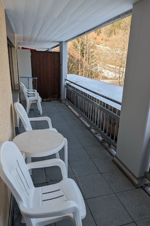 A covered outdoor area with a tiled floor, white plastic chairs, and a railing overlooking a snowy landscape. - Disentiserhof Haus C 102, (Disentis/Mustér), 1038 by Interhome (Disentis)