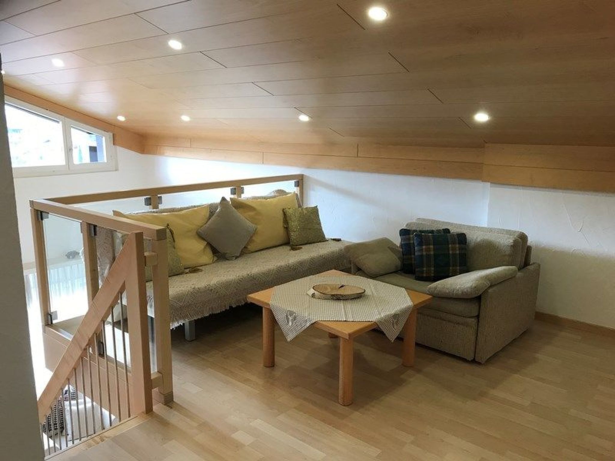 Ein gemütliches Wohnzimmer mit Holzboden, einer Couch, einem kleinen Sofa, einem Couchtisch und einer Treppe, die zu einer oberen Ebene führt.
