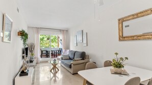 Ein modernes Wohnzimmer mit einer Couch, einem Esstisch, Stühlen, einem Balkon mit Tisch und Stühlen sowie einem großen, gerahmten Bild an der Wand.