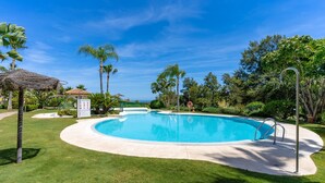 Ein Swimmingpool mit einer umlaufenden Rasenfläche, Palmen und blauem Himmel.