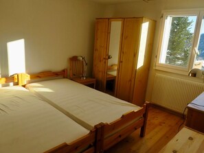 A bedroom with a wooden bed, a wardrobe, a desk, and a window with a view of trees. - Casa Segnas/Lindt, (Segnas), 1107 by Interhome (Disentis)