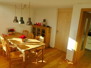 Ein Essbereich mit Holztisch und -stühlen, einem Schrank mit Glastüren sowie Pendelleuchten.