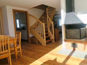 A spacious living area with a wooden staircase, a dining table with chairs, and a fireplace. - Casa Segnas/Lindt, (Segnas), 1107 by Interhome (Disentis)