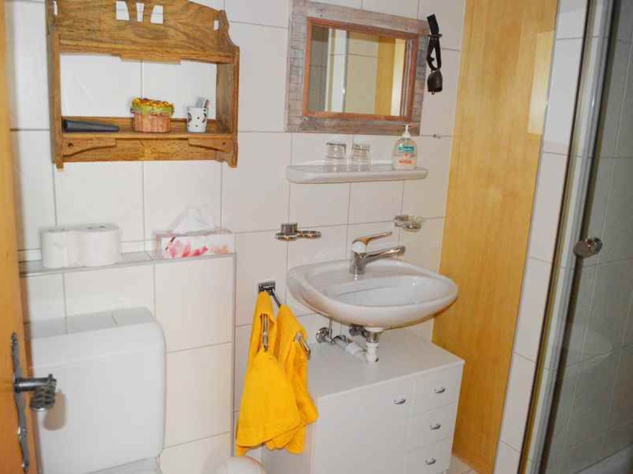 A bathroom with a white sink, a mirror above it, a toilet, and a towel rack with a yellow towel.