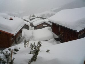 Ein verschneites Dorf mit Holzhäusern, einem Holzzaun und schneebedeckten Bäumen.
