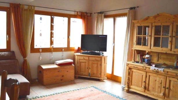 A living room with a television on a wooden cabinet, a sofa, a wooden cabinet with drawers, and a window with curtains. - Tgèsa Bostgé Grubenmann, (Sedrun), 154.01 by Interhome (Sedrun)