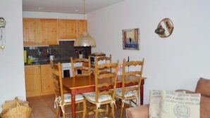 A dining area with wooden furniture, a kitchen in the background, and a wall with a framed picture and a decorative item. - Tgèsa Bostgé Grubenmann, (Sedrun), 154.01 by Interhome (Sedrun)