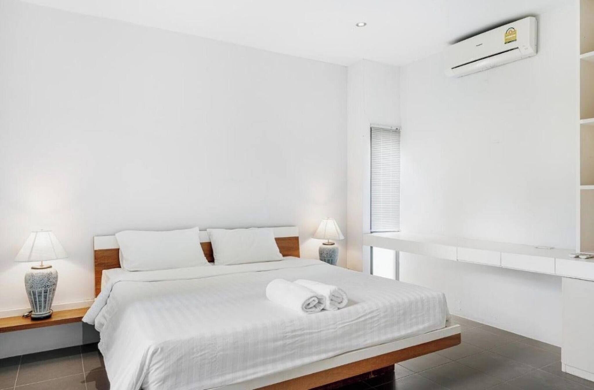 A modern hotel room with a bed, bedside tables, an air conditioning unit, and a window.