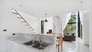 A modern kitchen with a marble countertop, a built-in sink, and a staircase leading to an upper level. - Room-ana's House in Lipa Noi (Koh Samui)