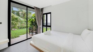 A bedroom with a large bed, a sliding glass door to a garden, and a view of greenery. - Room-ana's House in Lipa Noi (Koh Samui)