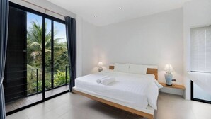 A modern bedroom with a large bed, two bedside lamps, and a view of greenery through a sliding door. - Room-ana's House in Lipa Noi (Koh Samui)