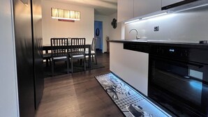 Een moderne keuken met een inbouwoven, een eethoek met een tafel en stoelen, en een hanglamp boven de tafel.