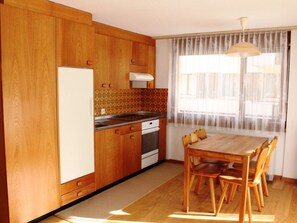 Eine Küche mit Holzausstattung, einem Kühlschrank, einem Herd und einem Esstisch mit Stühlen.