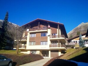 Ein mehrstöckiges Hotel mit Balkonen, im Hintergrund ein Ski-Hang und ein klarer, blauer Himmel.